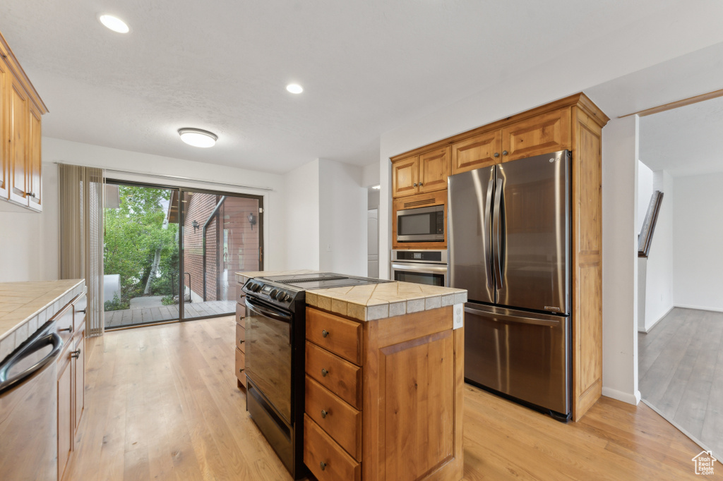 Kitchen featuring appliances with stainless steel finishes, tile countertops, light wood finished floors, a kitchen island, and recessed lighting
