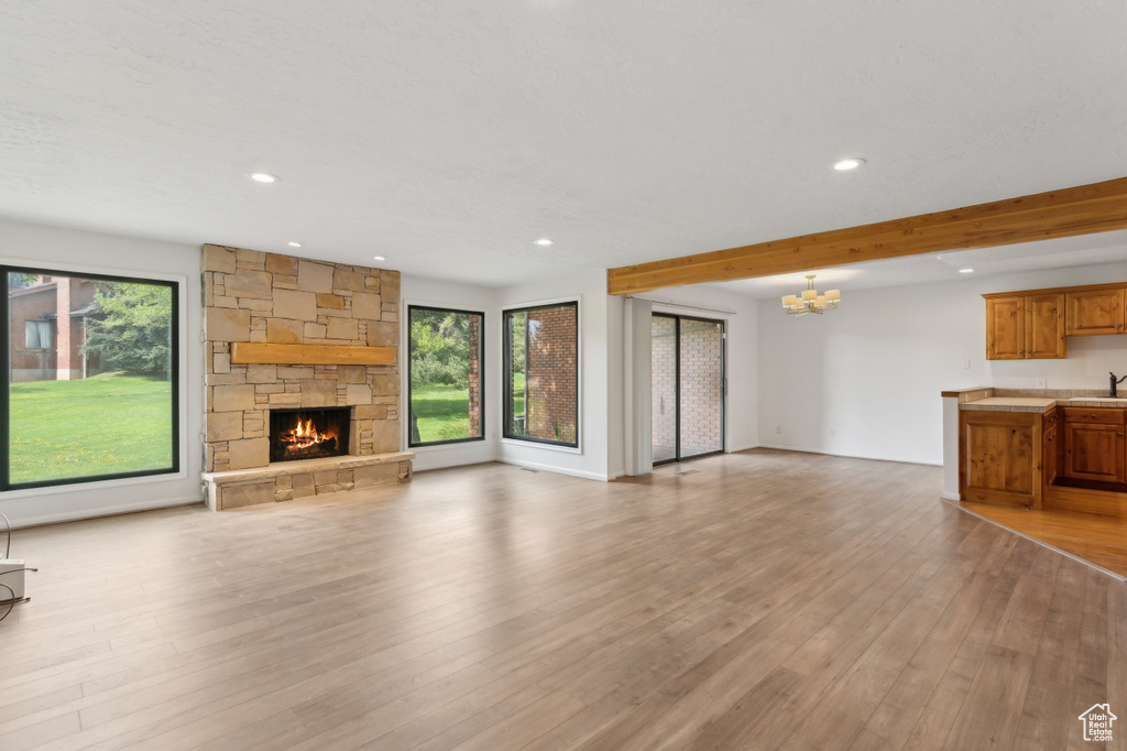 Unfurnished living room with healthy amount of natural light, a chandelier, recessed lighting, a stone fireplace, and light wood-style floors