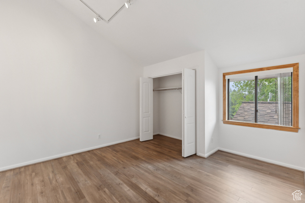 Unfurnished bedroom featuring vaulted ceiling, wood finished floors, baseboards, and a closet