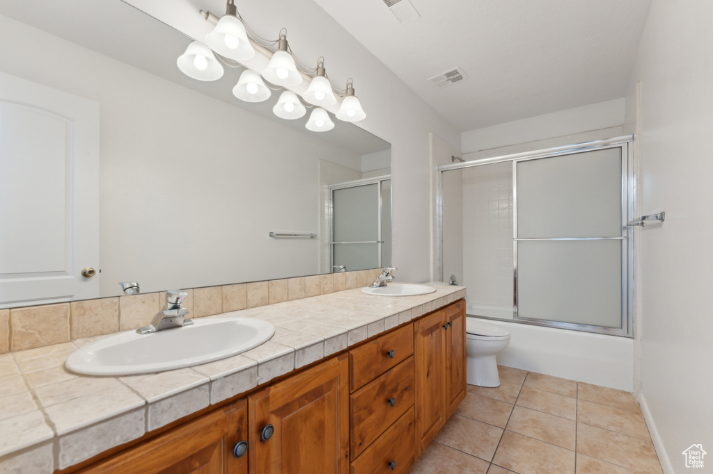 Full bathroom featuring toilet, tile patterned flooring, double vanity, and bath / shower combo with glass door