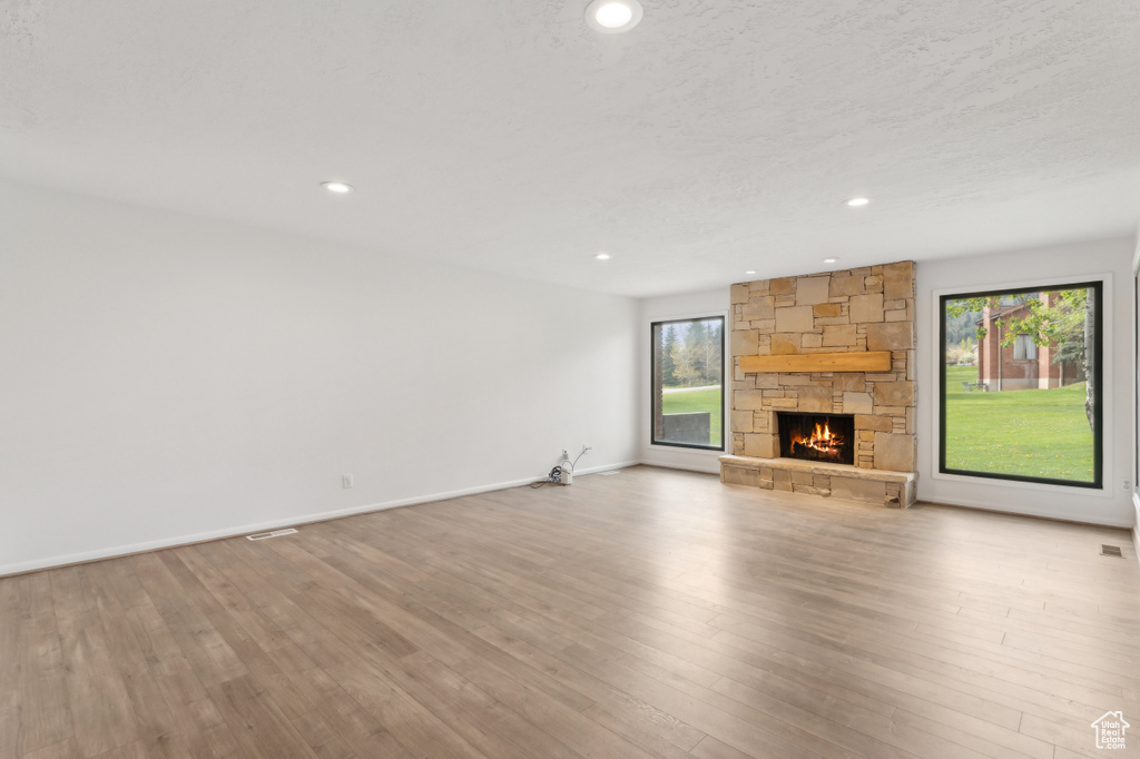 Unfurnished living room with a stone fireplace, recessed lighting, wood finished floors, and baseboards
