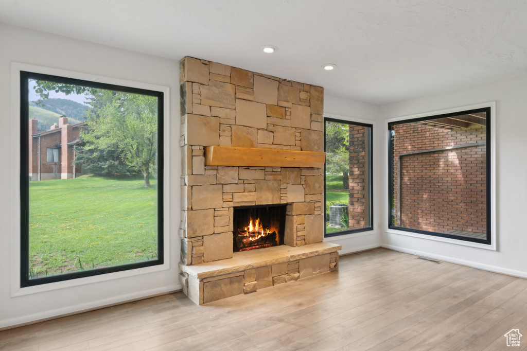 Unfurnished living room with a stone fireplace, wood finished floors, and baseboards