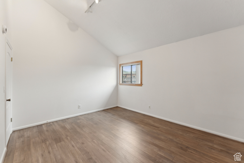 Empty room featuring lofted ceiling, wood finished floors, and baseboards