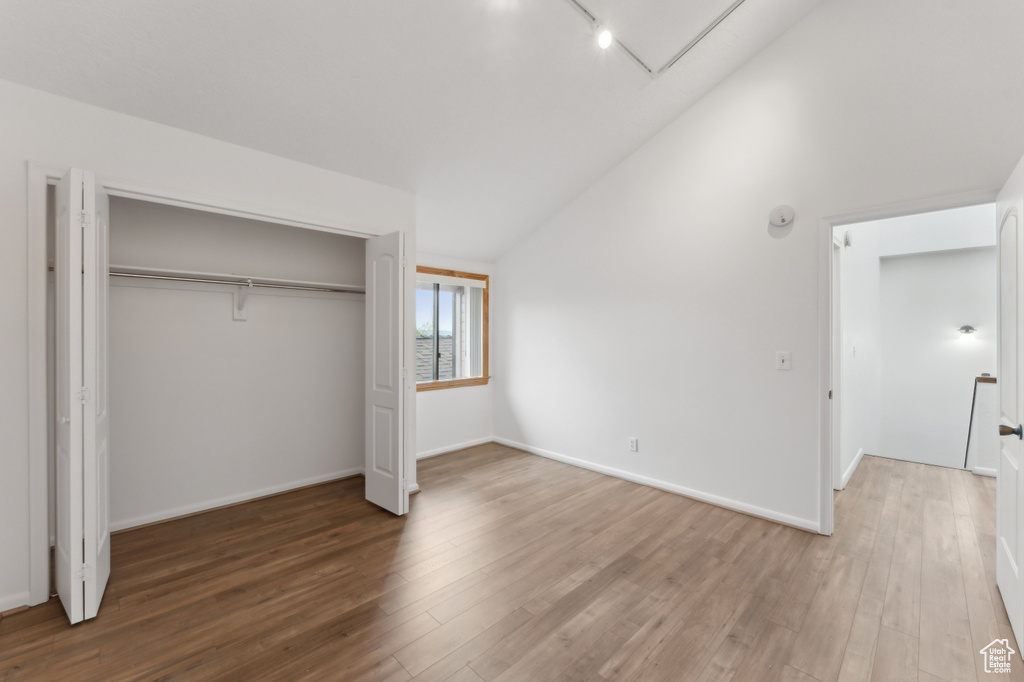 Unfurnished bedroom featuring vaulted ceiling, wood finished floors, a closet, track lighting, and baseboards