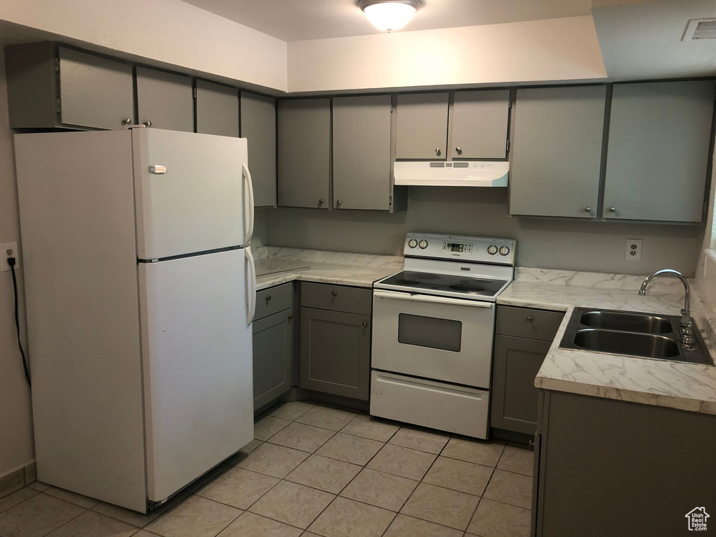 Kitchen with white appliances, a sink, under cabinet range hood, gray cabinets, and light tile patterned floors