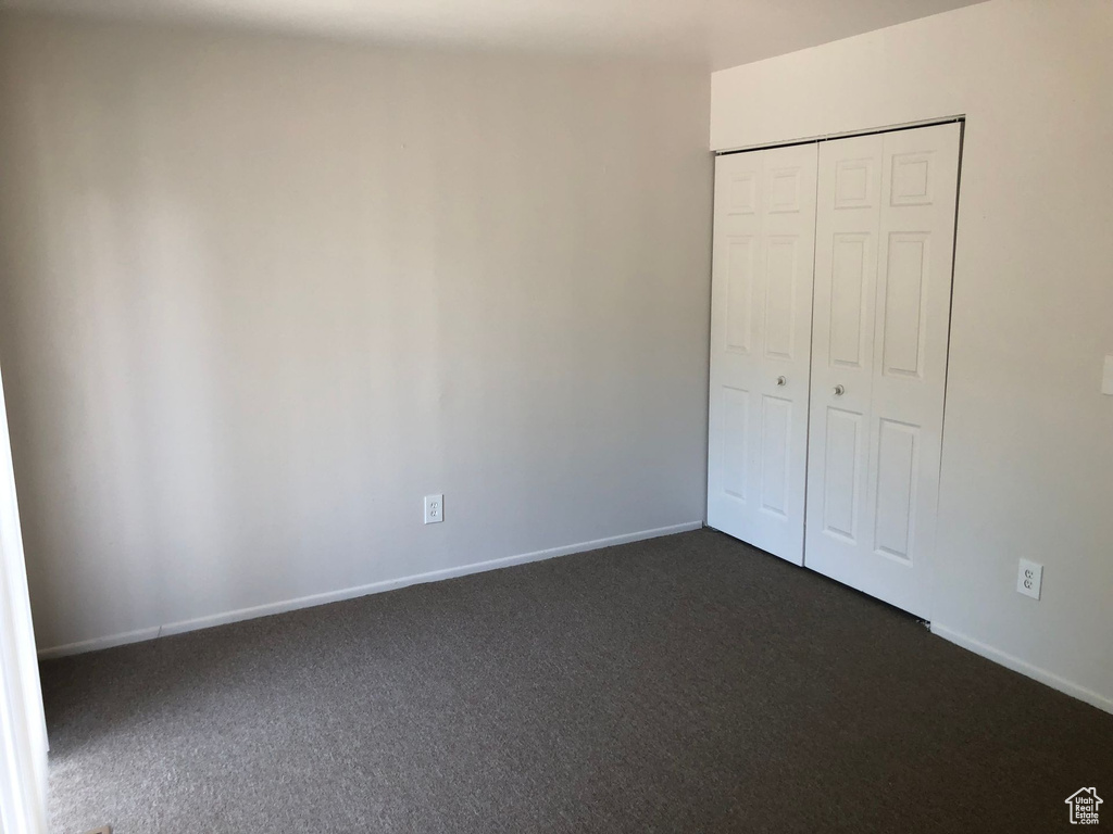 Unfurnished bedroom featuring dark colored carpet, baseboards, and a closet