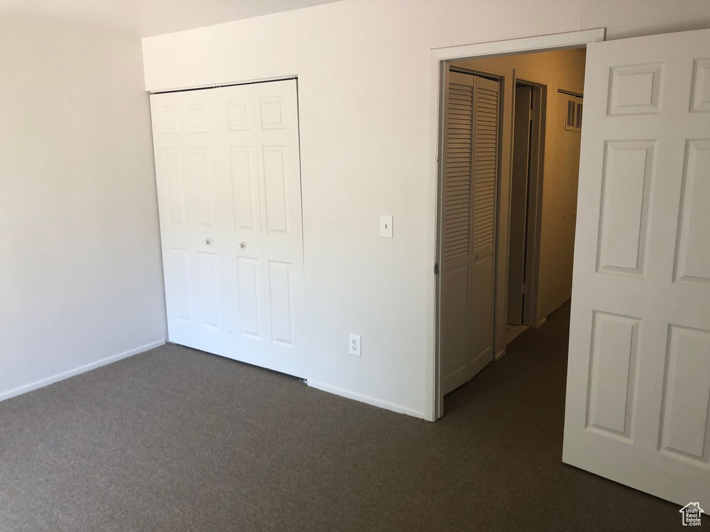 Unfurnished bedroom with dark colored carpet and baseboards