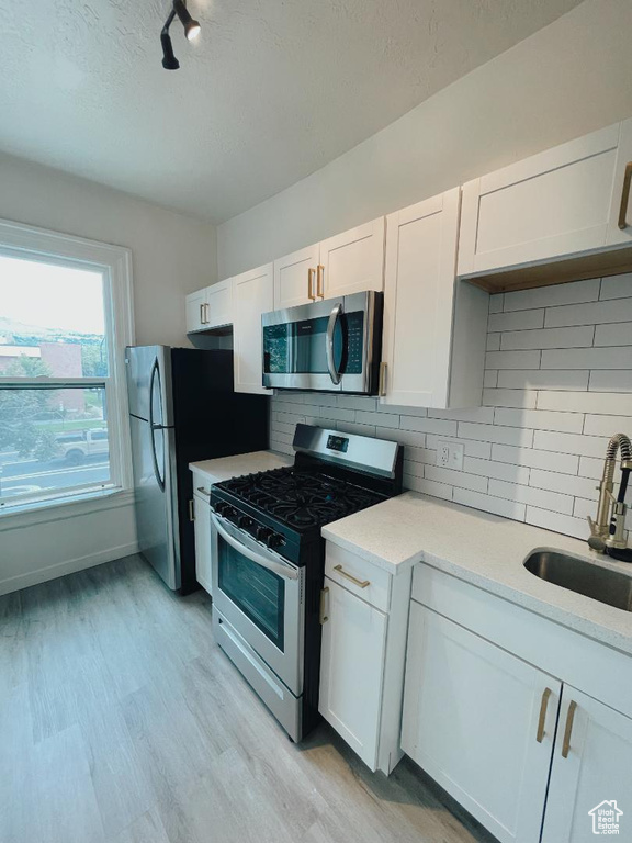 Kitchen with stainless steel appliances, a sink, light countertops, white cabinets, and a textured ceiling