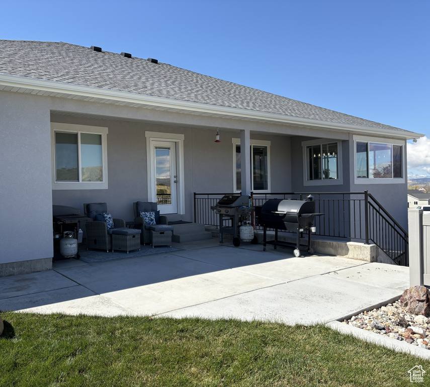 Back of property featuring a shingled roof, stucco siding, and an outdoor hangout area