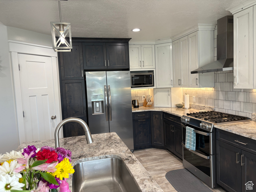 Kitchen featuring appliances with stainless steel finishes, wall chimney exhaust hood, a sink, light wood-style floors, and tasteful backsplash