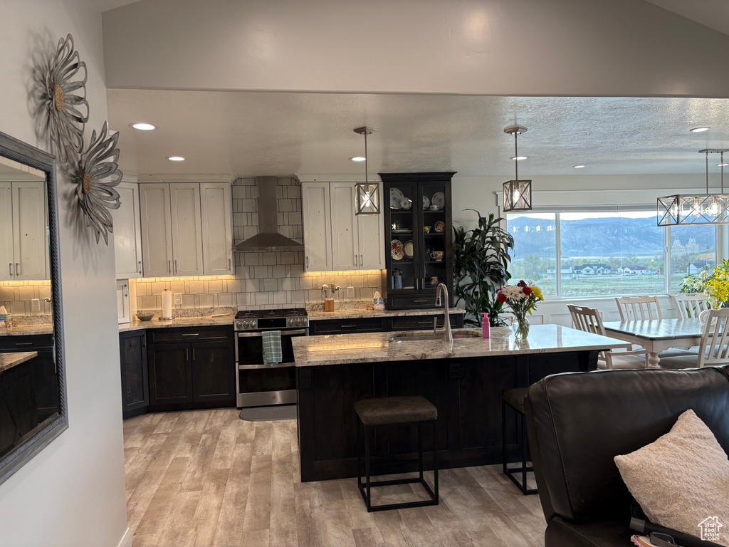 Kitchen featuring range with two ovens, wall chimney exhaust hood, a sink, a kitchen breakfast bar, and light stone countertops