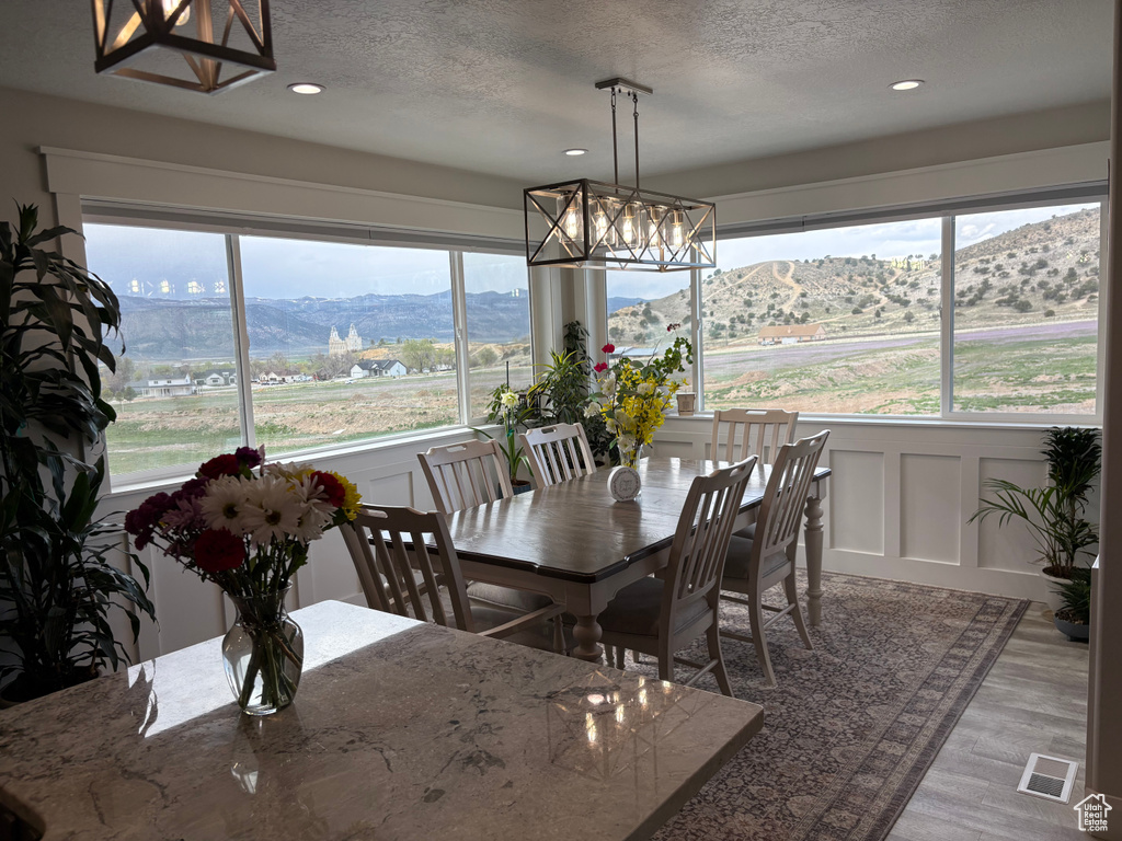 Dining space featuring a chandelier, plenty of natural light, a decorative wall, a textured ceiling, and wood finished floors