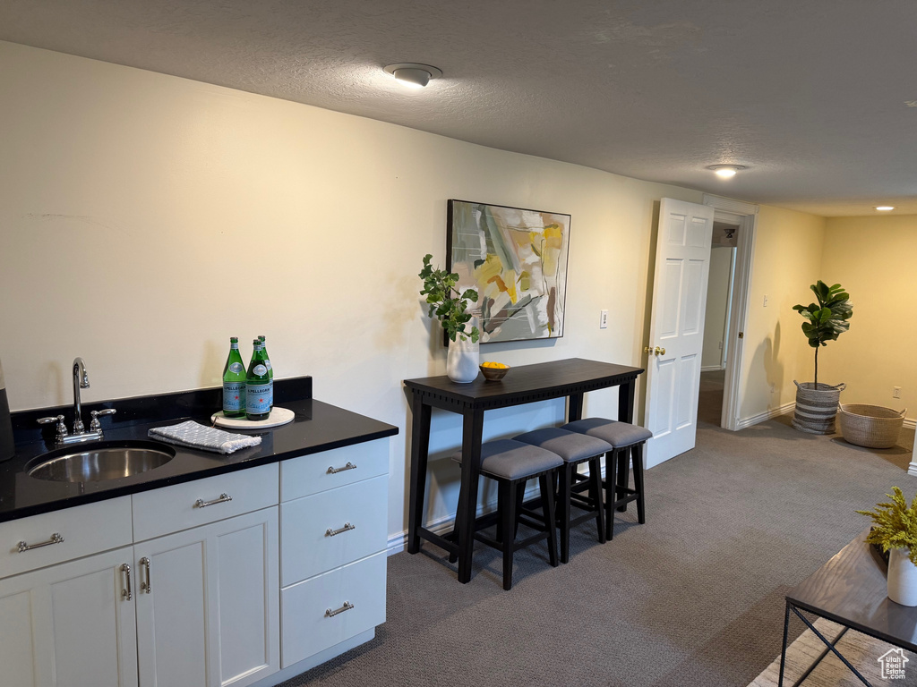 Kitchen with a sink, dark carpet, dark countertops, white cabinetry, and baseboards