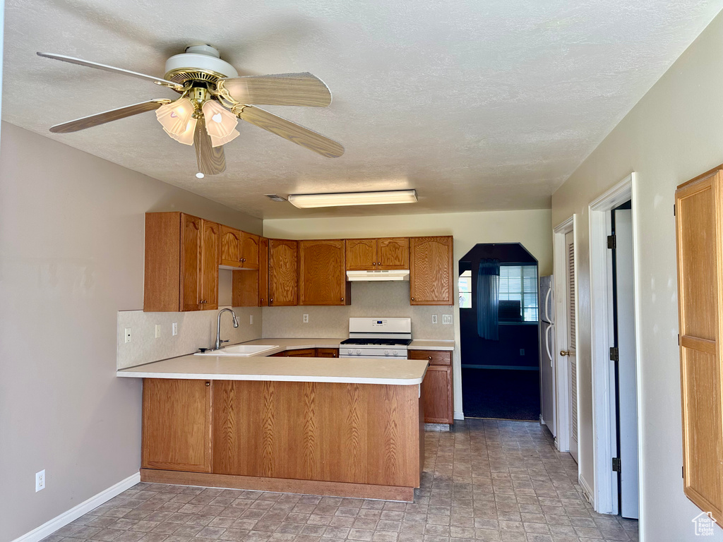 Kitchen featuring white gas range oven, a sink, under cabinet range hood, a peninsula, and light countertops