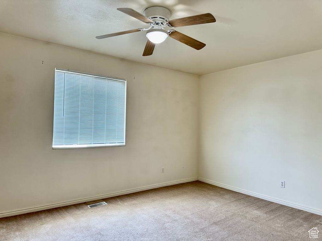 Carpeted empty room featuring a ceiling fan and baseboards