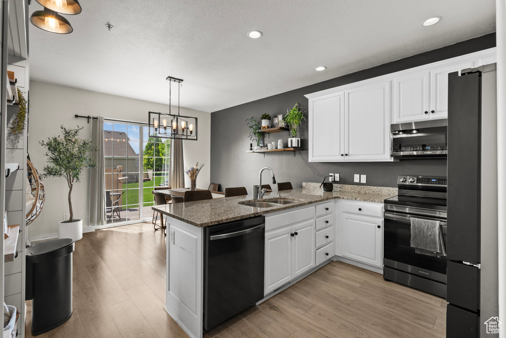 Kitchen featuring stainless steel appliances, a sink, open shelves, a peninsula, and light wood finished floors