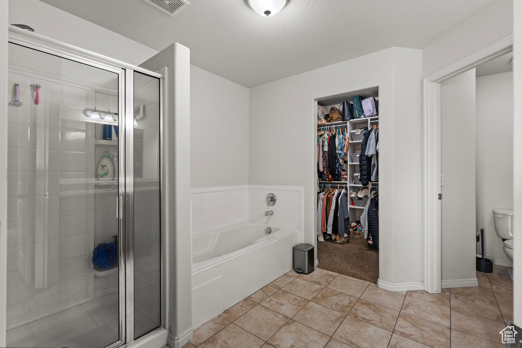 Bathroom featuring a stall shower, toilet, a bath, a spacious closet, and tile patterned floors