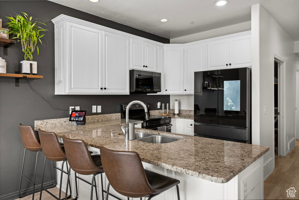 Kitchen featuring black appliances, a sink, a peninsula, white cabinets, and recessed lighting