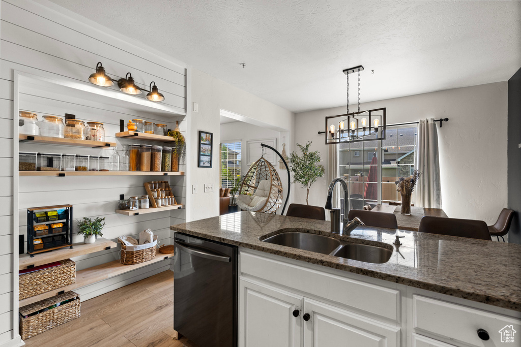 Kitchen with dishwashing machine, a sink, light wood-style flooring, dark stone countertops, and a chandelier
