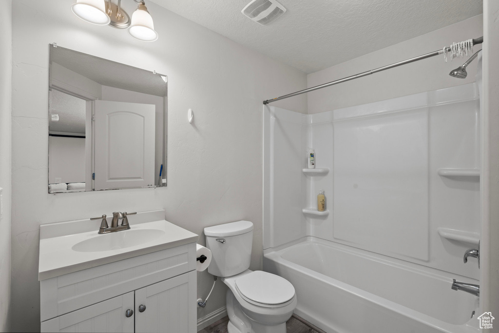 Bathroom featuring a textured ceiling, vanity, toilet, and tub / shower combination