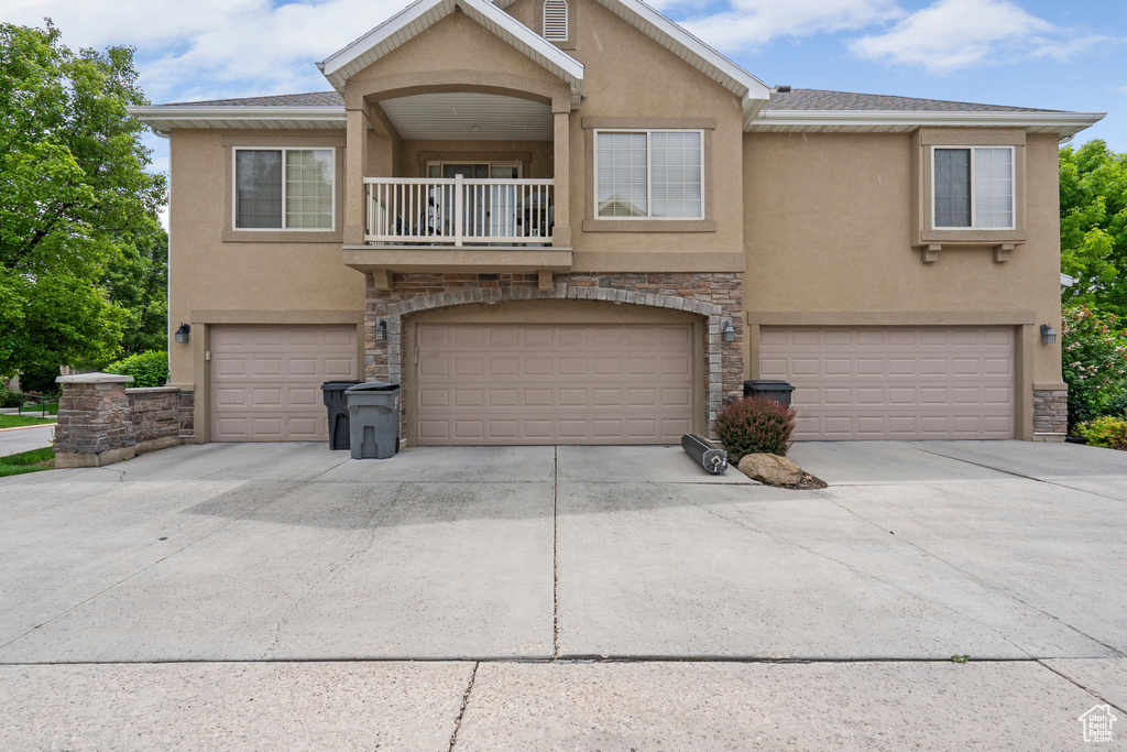 View of front facade featuring stucco siding, a balcony, a garage, stone siding, and concrete driveway