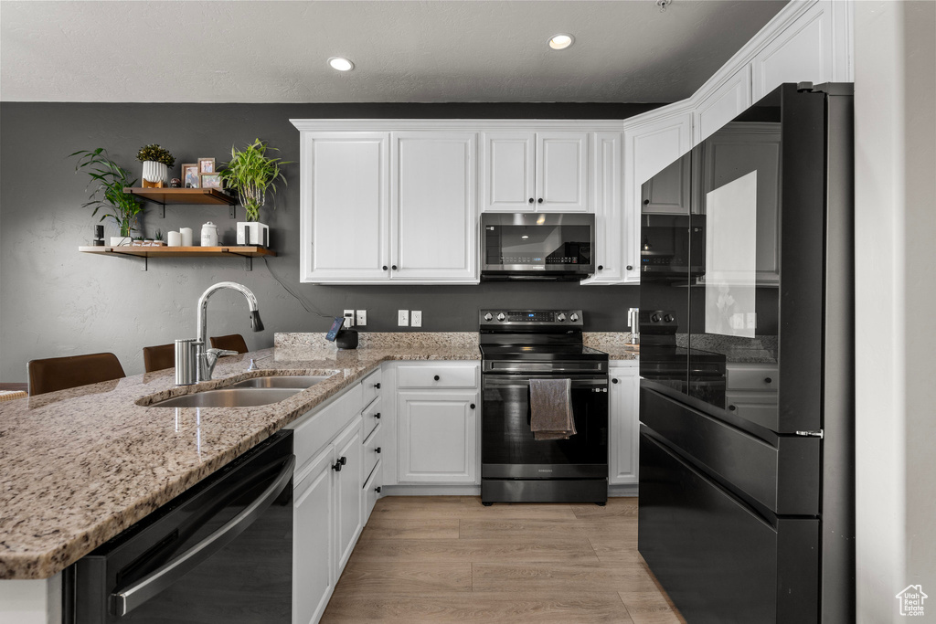 Kitchen featuring black appliances, a sink, white cabinetry, recessed lighting, and light stone counters