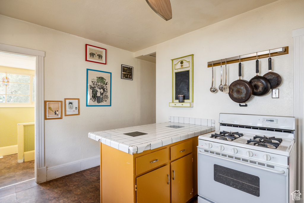 Kitchen with white range with gas stovetop, a peninsula, baseboards, and tile countertops