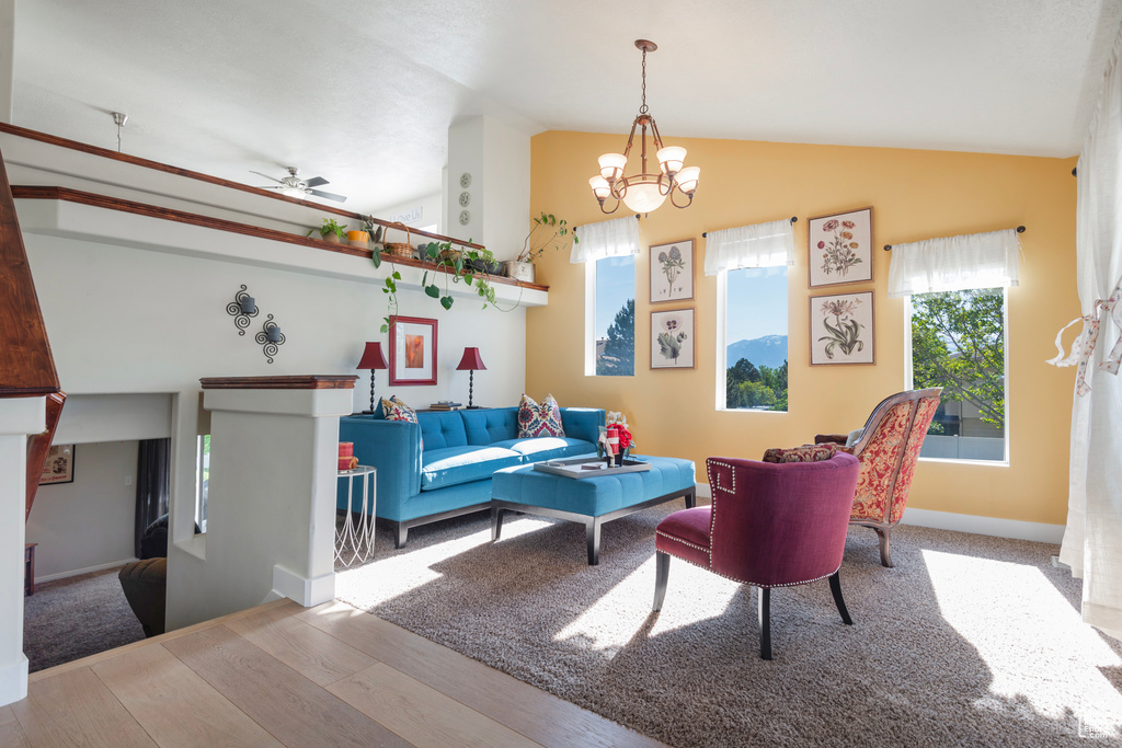 Living area with vaulted ceiling, wood finished floors, a chandelier, ceiling fan, and baseboards