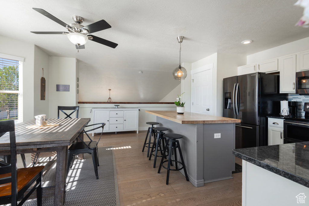 Kitchen with stainless steel appliances, white cabinetry, butcher block countertops, a center island, and a kitchen breakfast bar