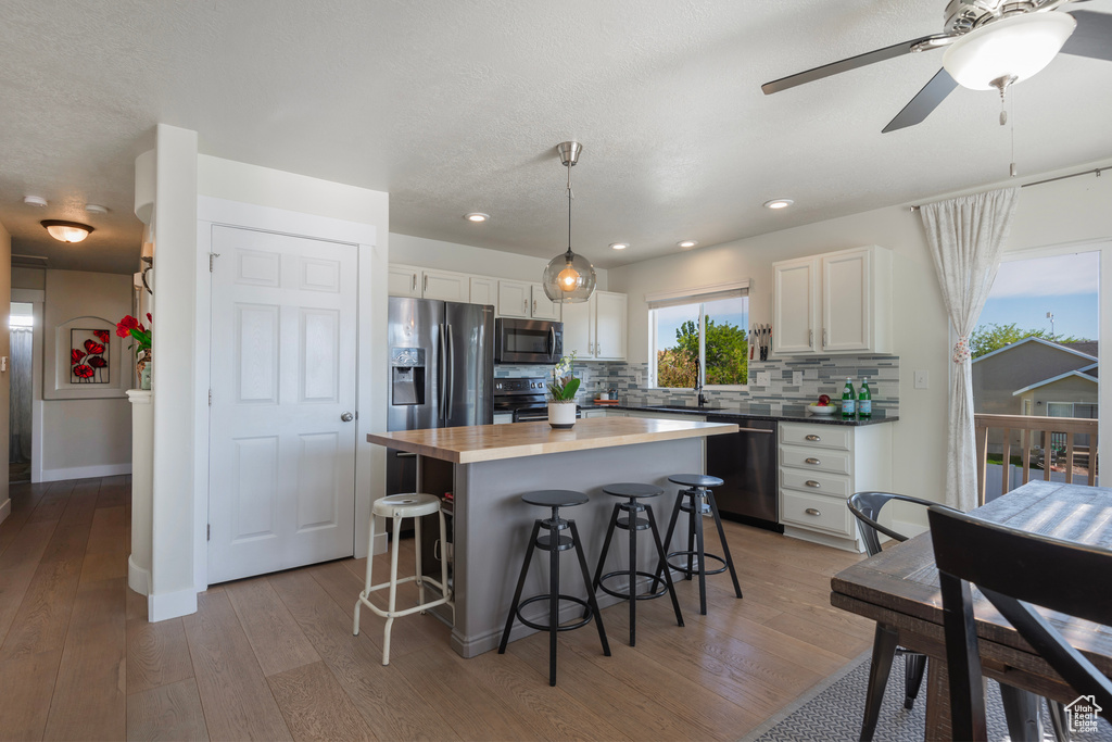 Kitchen featuring stainless steel appliances, white cabinetry, a kitchen bar, light wood-type flooring, and recessed lighting