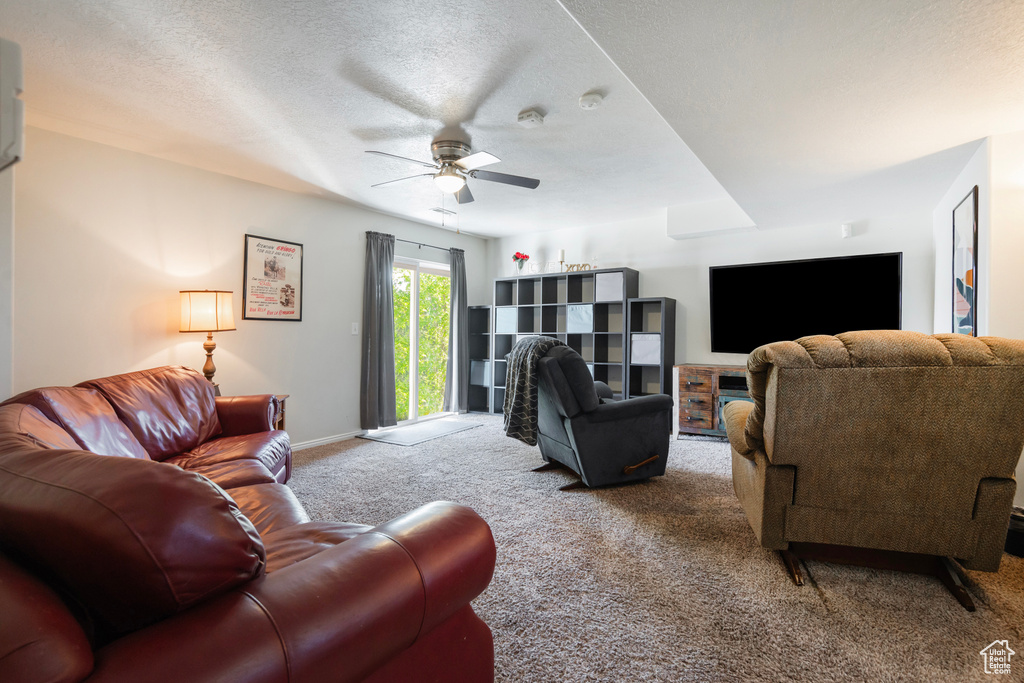 Carpeted living room featuring ceiling fan, baseboards, and a textured ceiling