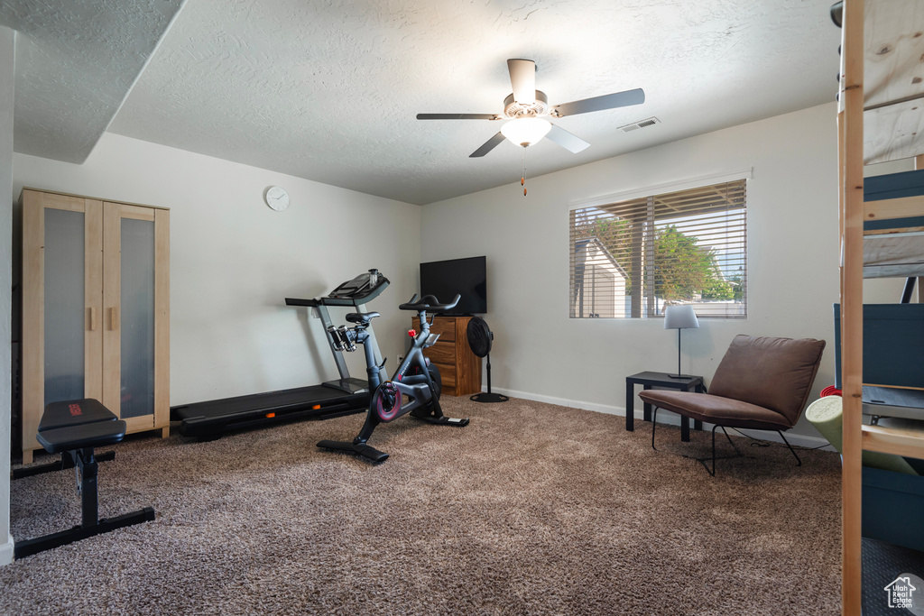 Exercise area featuring ceiling fan, a textured ceiling, carpet floors, and baseboards