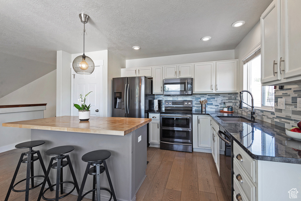 Kitchen featuring appliances with stainless steel finishes, wooden counters, a sink, a breakfast bar, and white cabinets