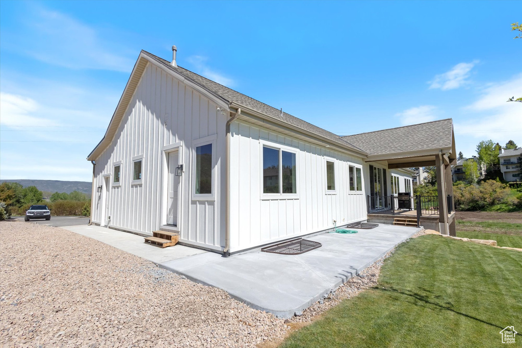 Back of property with board and batten siding, roof with shingles, a lawn, and a patio area