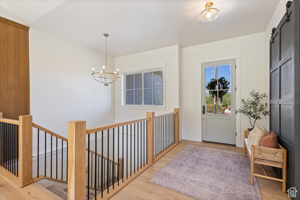 Foyer with a barn door, wood finished floors, and a chandelier
