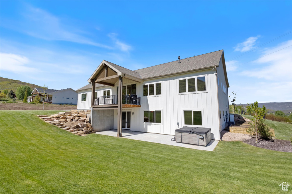 Back of house featuring a hot tub, a balcony, a patio area, board and batten siding, and a yard