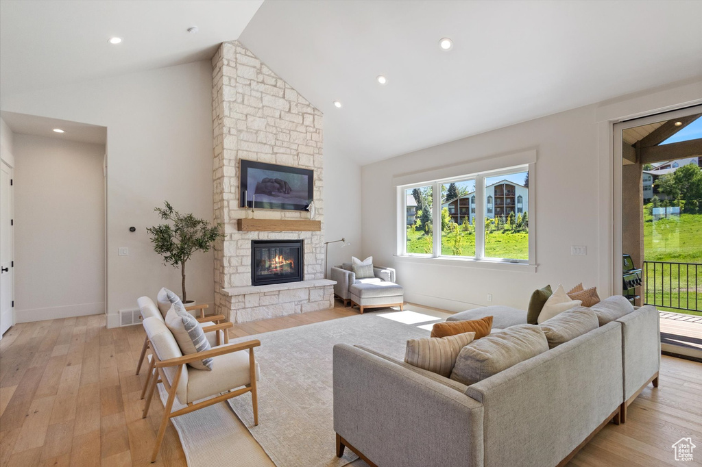 Living room featuring a stone fireplace, plenty of natural light, light wood-style floors, high vaulted ceiling, and recessed lighting