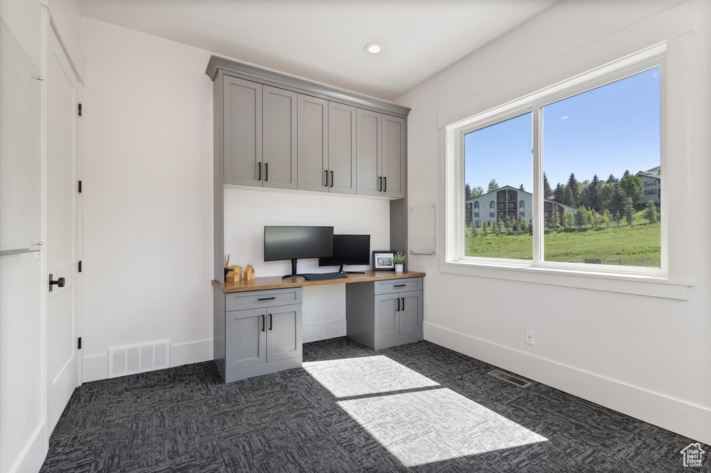 Office space featuring built in desk, baseboards, dark colored carpet, and recessed lighting