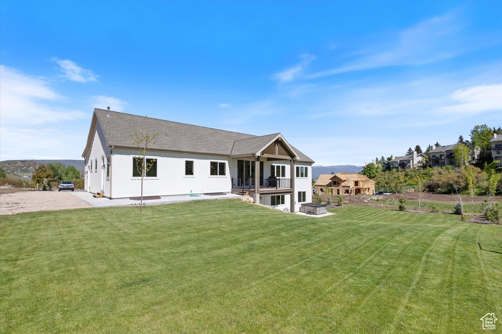 Back of house featuring a lawn, a balcony, and a shingled roof