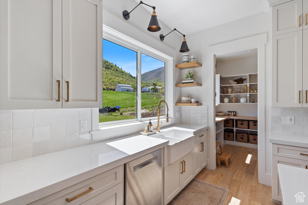 Kitchen with stainless steel dishwasher, a sink, decorative backsplash, light wood finished floors, and light countertops