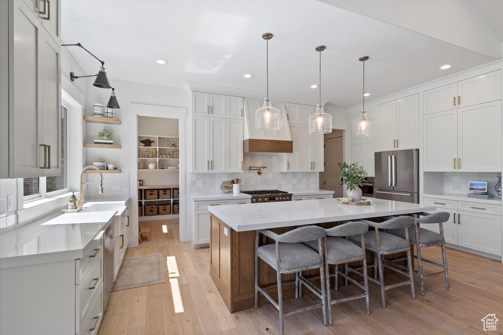 Kitchen featuring high end fridge, tasteful backsplash, light wood finished floors, a breakfast bar area, and recessed lighting