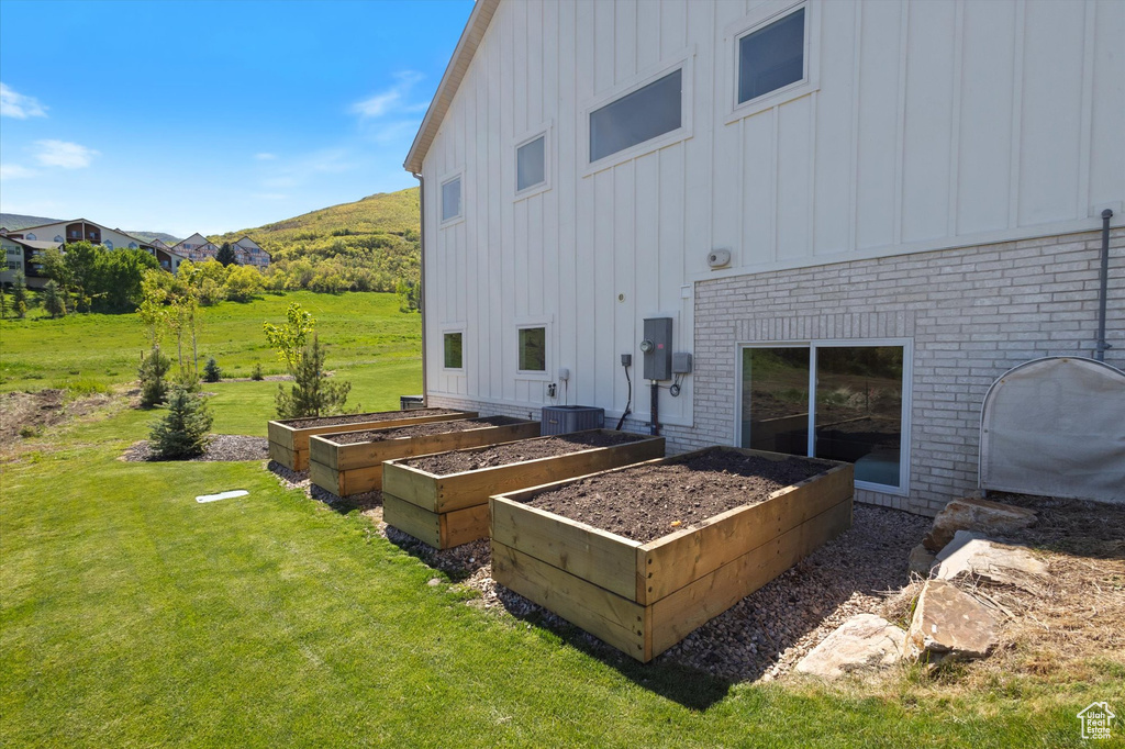 Back of property featuring board and batten siding, a lawn, a garden, brick siding, and central AC unit