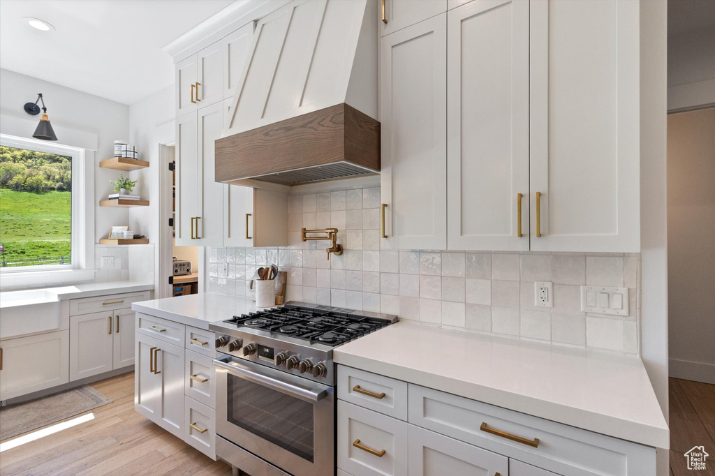 Kitchen with high end stainless steel range, custom range hood, light countertops, light wood finished floors, and recessed lighting