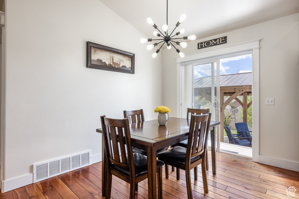 Dining area with a chandelier, wood-type flooring, baseboards, and lofted ceiling