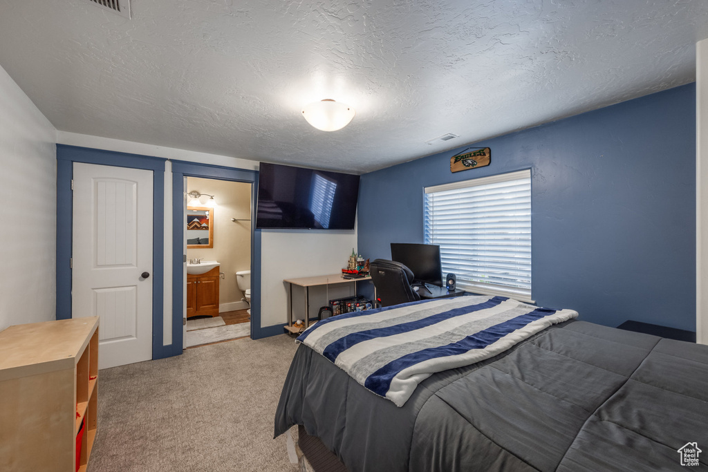 Bedroom with light colored carpet, a textured ceiling, and connected bathroom