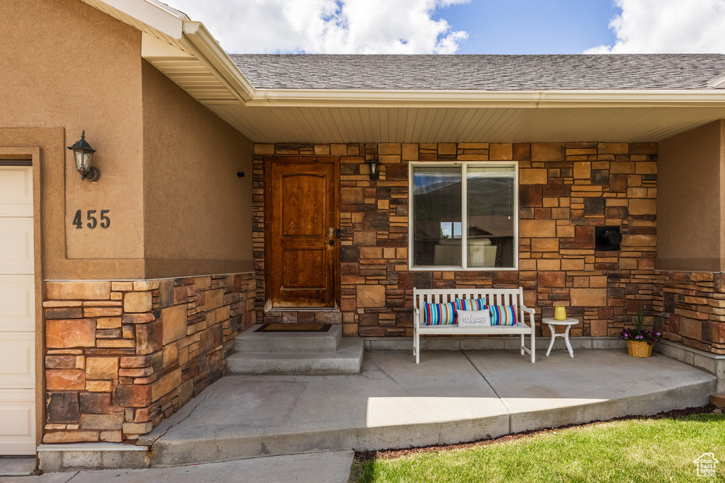 Doorway to property with stone siding, covered porch, and a shingled roof