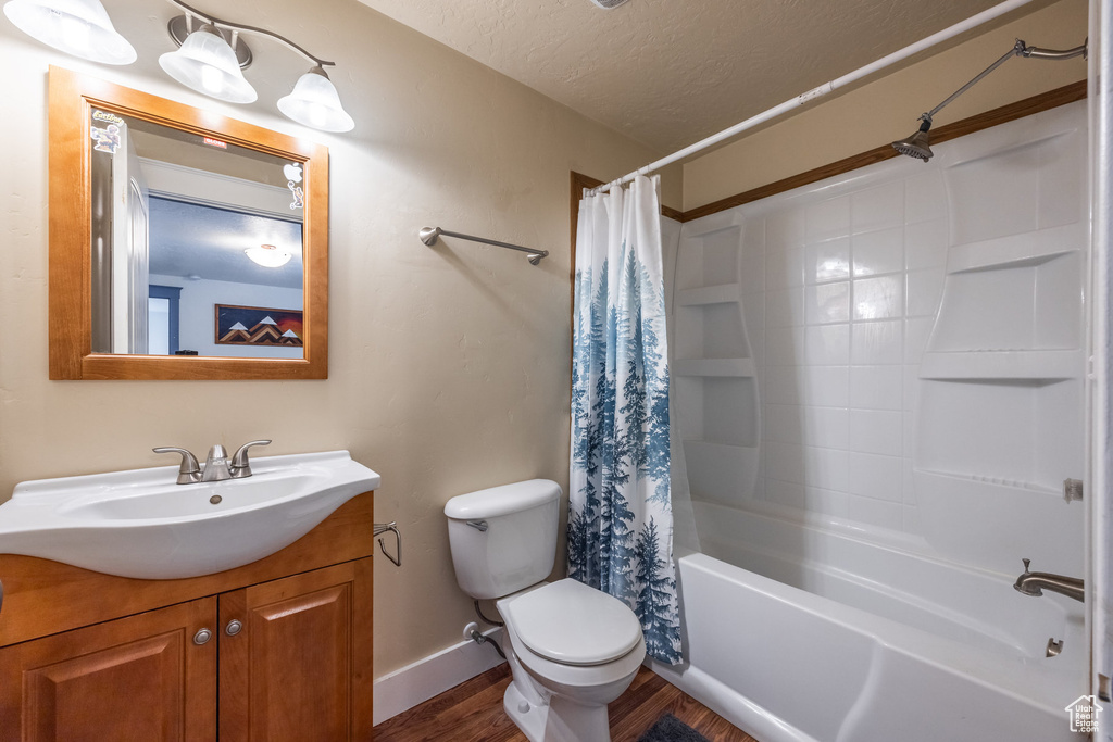 Bathroom with wood finished floors, vanity, toilet, shower / bathtub combination with curtain, and a textured ceiling