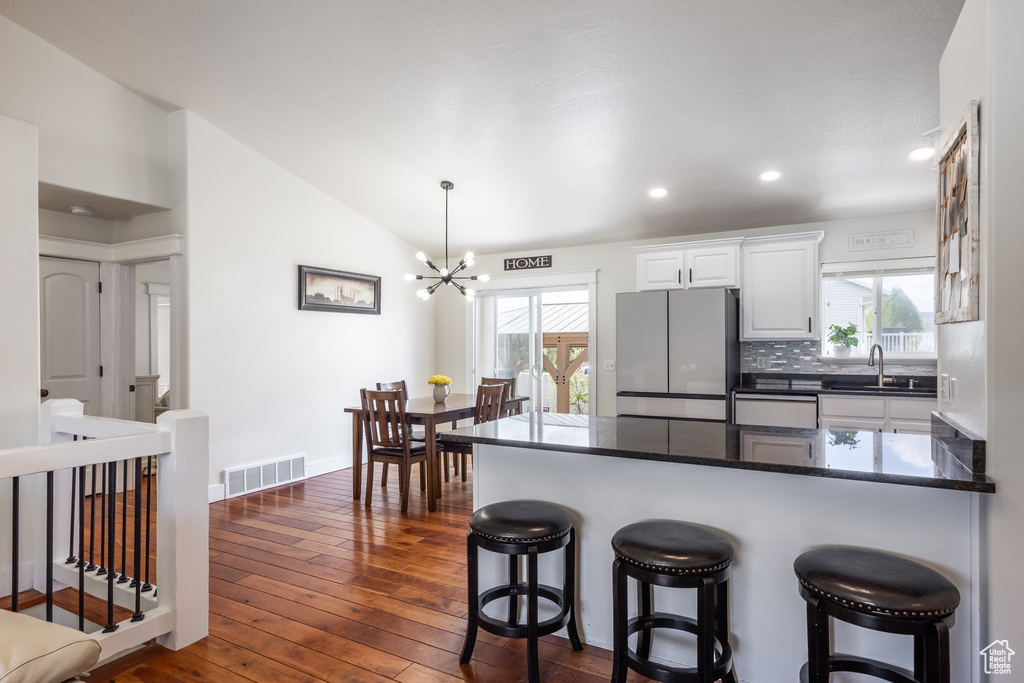 Kitchen featuring freestanding refrigerator, a sink, a chandelier, vaulted ceiling, and a peninsula