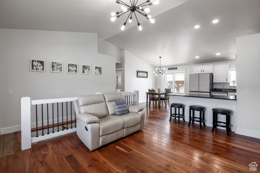 Living area featuring a chandelier, vaulted ceiling, dark wood-style floors, baseboards, and recessed lighting
