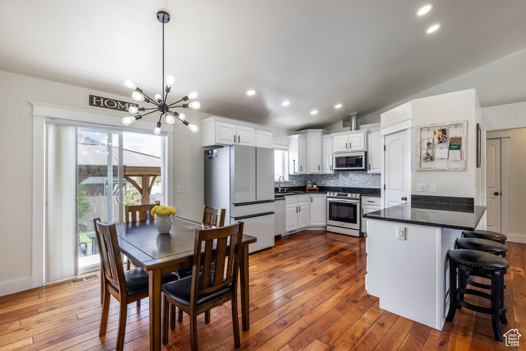 Kitchen with stainless steel appliances, a peninsula, a chandelier, dark wood-style flooring, and vaulted ceiling